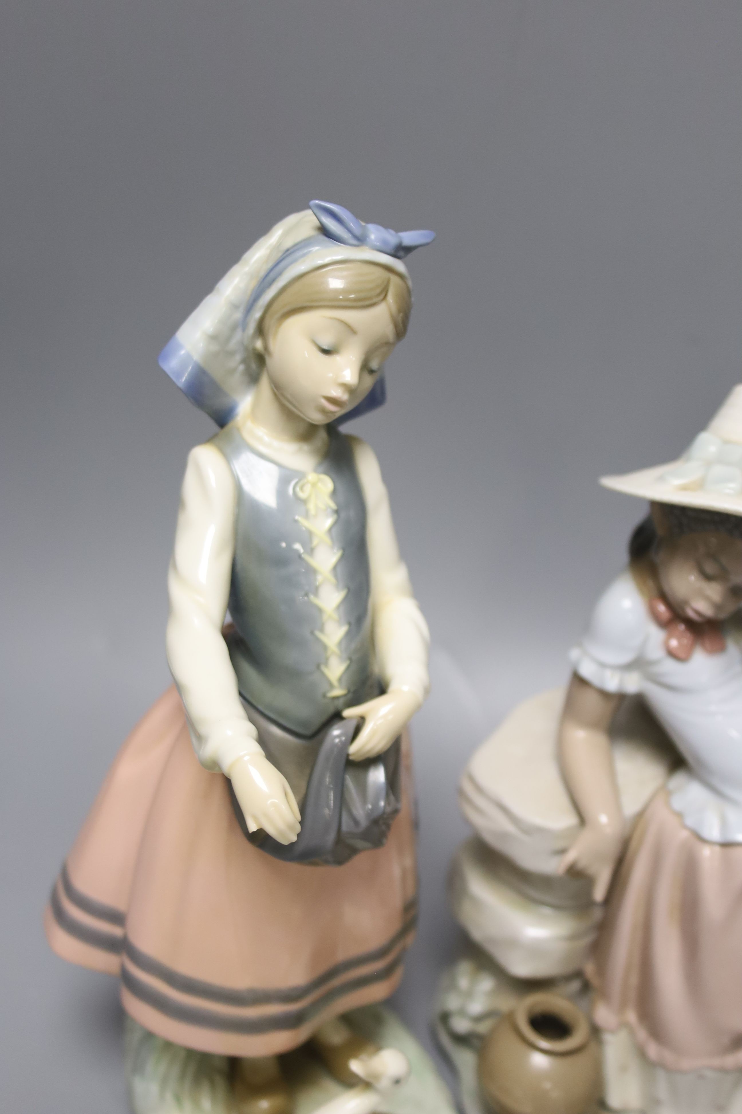 A Lladro figure of a girl feeding a duck, another sitting on a wall, and a girl with two ducks, tallest 26cm